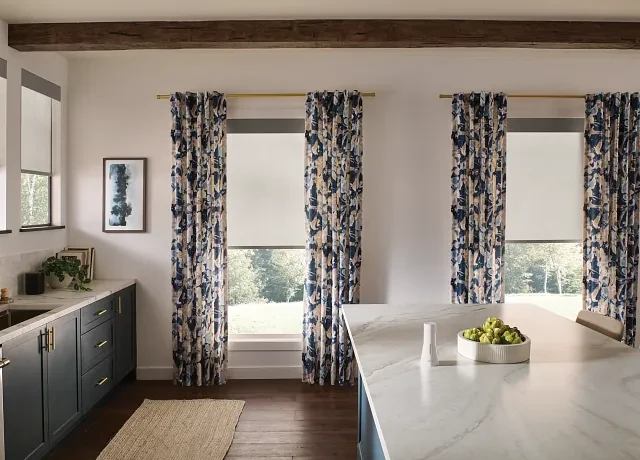 Graber light-filtering roller shades layered with patterned blue drapery in a bright kitchen.