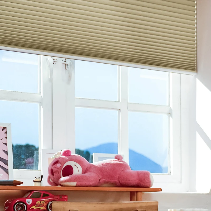 Beige SmartWings Nowa cellular shade partially lowered over a white-framed window above a shelf of toys.